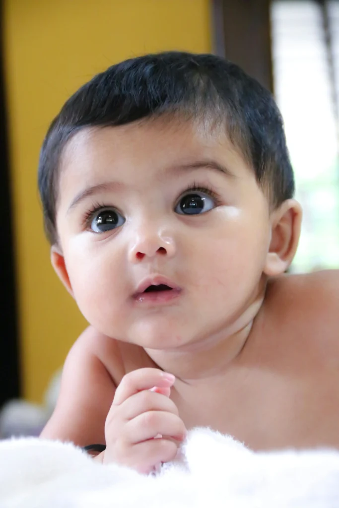 cute baby with big eyes and short black hair, looking curiously while resting on a soft surface