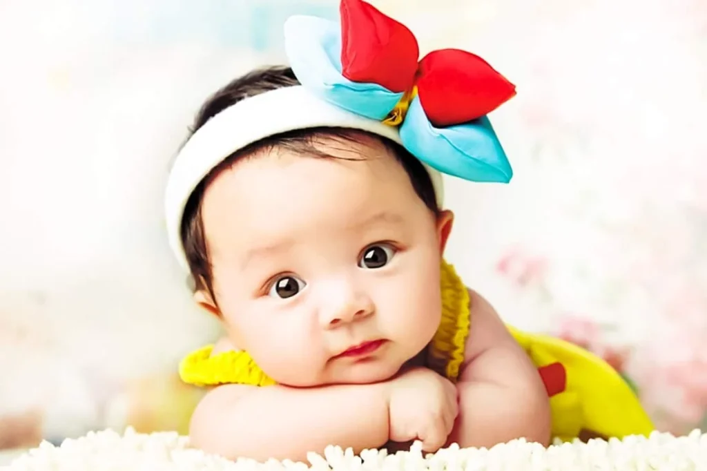 cute baby with a large bow, resting on a soft surface, looking curiously at the camera