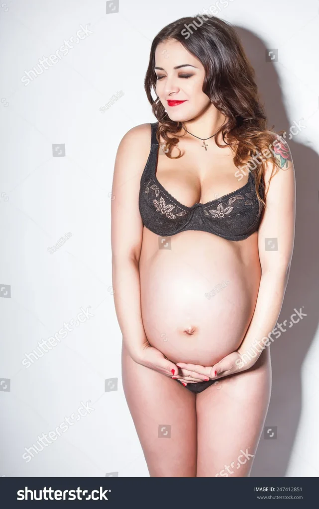 pregnant woman in black lingerie gently cradling her belly, smiling softly against a light background