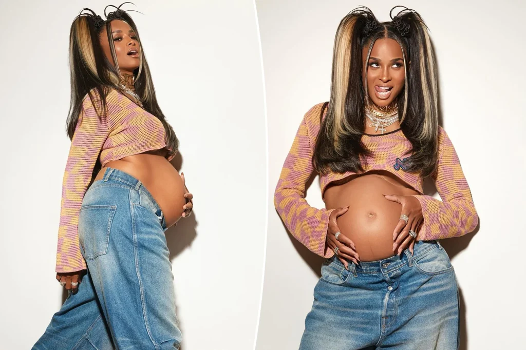 Pregnant woman in a cropped sweater and baggy jeans, showcasing her belly with a confident pose.